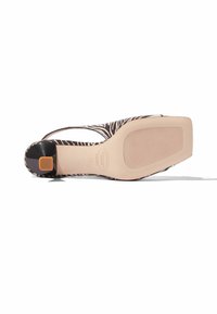 Scarpa con tacco alto a motivo zebra, con un'accenno nero sul tacco, dotata di una suola beige liscia e un design con ritagli per la ventilazione.