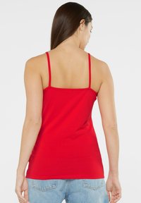 Red tank top with thin straps, fitted design, stretch cotton material. Smooth texture, simple hemline, worn with light blue high-waisted jeans.
