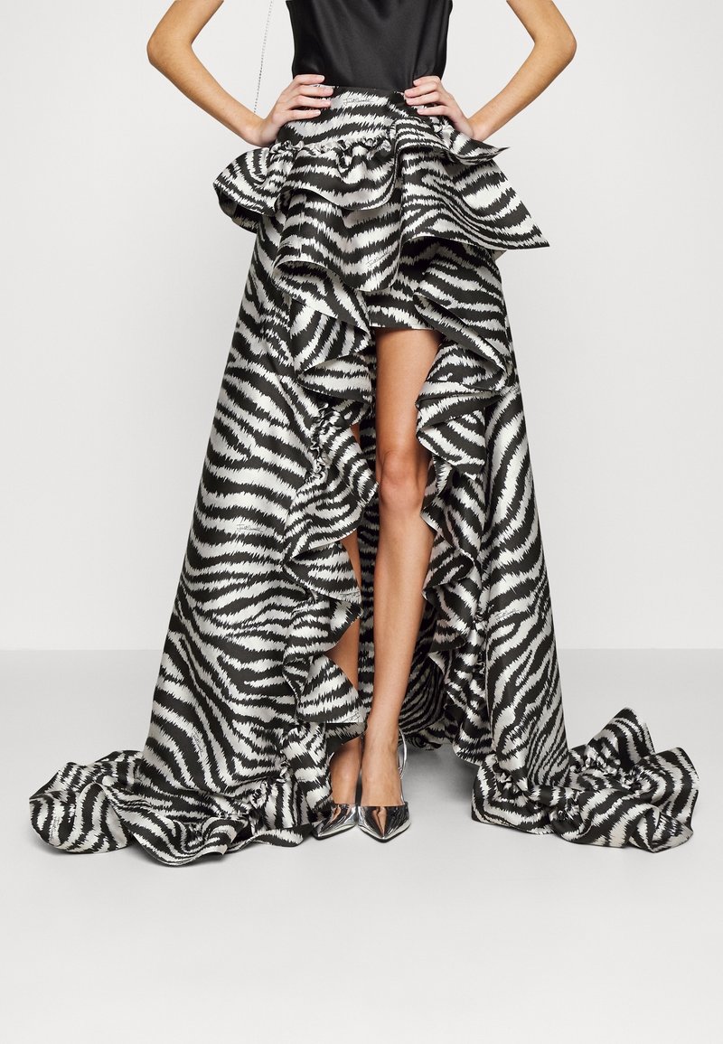 Randig kjol med zebramönster i svart och vitt, med hög slits och kaskadlager, samt metalliska spetsiga skor. Slät tygtextur.