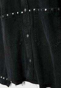 Schwarzes Jeanshemd mit Metall-Druckknöpfen, zwei Brusttaschen, jeweils mit silbernen Nieten besetzt, und einem ausgefransten Saum.