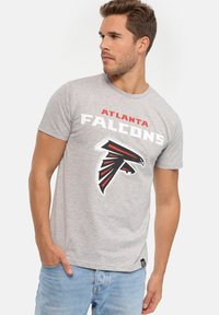Šedé tričko s krátkým rukávem, na kterém je nápis "Atlanta Falcons" a logo sokola v černé, červené a bílé barvě. Materiál bavlna, pohodlný střih.