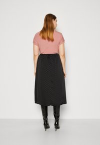 Rosa kortermet topp paret med et svart, kne-langt skjørt med vertikale striper, komplettert med høye, blanke svarte støvler.
