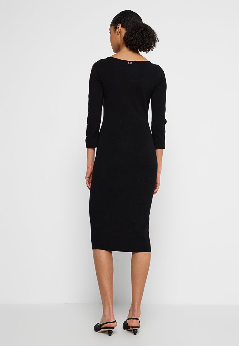 Zwarte jurk van gemiddelde lengte met driekwart mouwen, gebreide textuur en een ronde rug met een kleine gouden acccent.