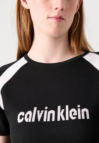 Juodas prisitaikantis megztinis su baltais horizontaliais raštais ant pečių ir "calvinklein" tekstu šviesiame šriftu. Lygus apykaklė.