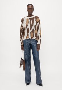 Brown and white patterned knit sweater with long sleeves, paired with blue wide-leg jeans and a small brown fringe bag. Black pointed shoes.