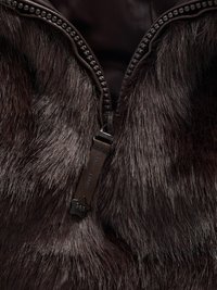 Καφέ ύφασμα από ψεύτικη γούνα με απαλό υφή, διαθέτοντας λεπτομέρεια με φερμουάρ και ετικέτα. Το φερμουάρ είναι σκούρο με ομαλό μηχανισμό κλεισίματος.