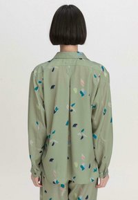 Langärmliges Hemd aus leicht grünem Stoff mit bunten, abstrakten Blattmustern, ausgestattet mit einem Button-Down-Kragen und einem lässigen Schnitt.