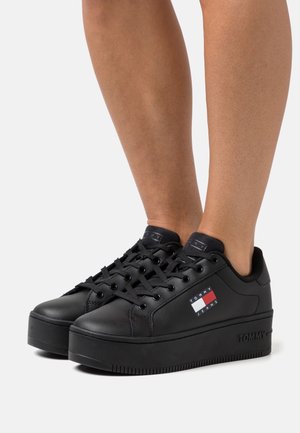 Mustat platfrom-tyyliset tennarit, joissa on sileä nahkapinta, pyöreä kärki ja mustat nauhat. Koristettu pienellä brändillä varustetulla merkintälaatikolla, jossa on punaisia, valkoisia ja sinisiä yksityiskohtia.