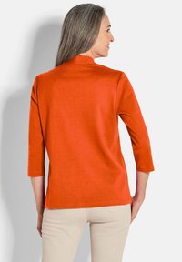 Oranje driekwart mouw top van zachte stof met een hoge halslijn, gladde textuur en eenvoudige, strakke snit, gecombineerd met beige broeken.