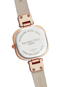 Reloj cuadrado con fondo de acero inoxidable, caja de metal en oro rosa, correa de cuero genuino en color beige y detalles grabados que incluyen el nombre de la marca.