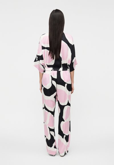 Luftig jumpsuit med blommönster i rosa, svart och vitt, med insvängd midja och vida ärmar, tillverkad av ett mjukt tyg.