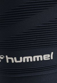 Granatowa, sportowa rękawica z teksturowanymi poziomymi paskami i białym logo "hummel". Wykonana z elastycznego, oddychającego materiału.