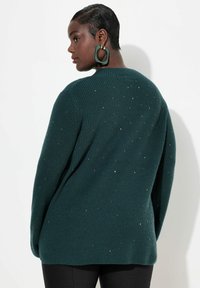 Grön ribbad tröja med spridda metalliska accenter, med avslappnad passform, rund halsringning och långa ärmar. Mjuk textur, bakvy visas.