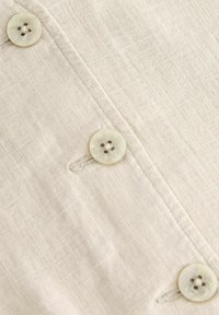 Tela de lino beige claro con una textura sutil, con botones de color claro y un diseño relajado de cierre con botones.