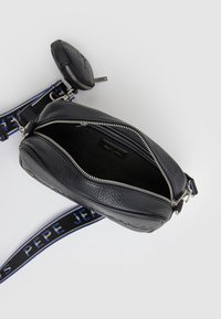 Bolso negro de cuero cruzado de forma redondeada, con una cremallera plateada, un compartimento abierto y una correa ajustable con un patrón.