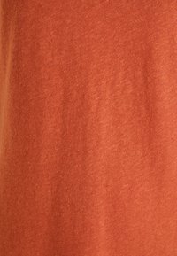 Gros plan sur un tissu doux de couleur rouille avec un motif tricoté fin légèrement texturé.