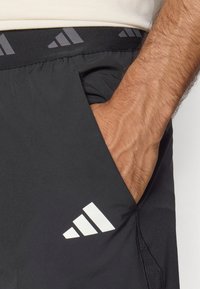 Mustad mustrisportlikud lühikesed püksid pehme tekstuuriga, millel on hallide aktsentidega vöökoht ja valge logo alumises vasakus osas. Includes küljetaskud.