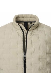 Beige gesteppte Jacke mit hohem Kragen, Reißverschluss vorne und schwarzem Zubehör. Besitzt dezente bedruckte Textdetails entlang des Reißverschlusses.