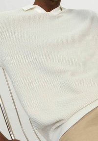 Bílý texturovaný pletený polo tričko s designem ve tvaru V a žebrovaným lemem. Má kontrastní světlý límec. Kruh tvarovaný s uvolněným střihem.