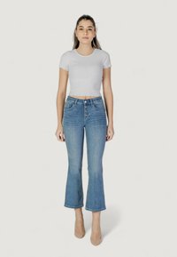 Top corto acanalado gris claro y jeans azul de cintura alta y corte acampanado con una fila de botones, que ofrecen un ligero estiramiento y un dobladillo deshilachado. Zapatos de tacón en tonos neutros.