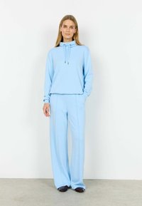 Hellblauer Sweatshirt mit hohem Kragen und Kordelzug, kombiniert mit passenden weiten Hosen, gefertigt aus weichem, strukturiertem Stoff.