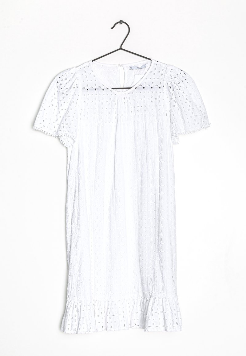 Vestido blanco de manga corta con patrón de ojales, cintura fruncida y dobladillo con volantes. Cuelga de un gancho negro contra un fondo sencillo.