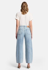 Ljust blå vida jeans med hög midja, fransad nederkant och en brun läderlapp på bakfickan, i kombination med en vit t-shirt.