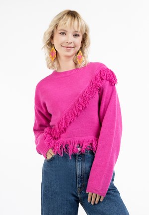 Fuchsia gestrickter Pullover mit diagonalen Fransen, runden Ausschnitt und langen Ärmeln, kombiniert mit hochgeschnittenen blauen Jeans.