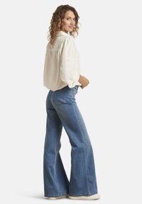 Blouse en crème clair avec un motif discret de cœurs, coupe décontractée et manches bouffantes, associée à un jean bleu flared taille haute.