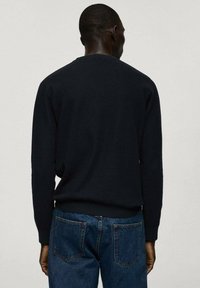 Pulover tricotat de culoare bleumarin, cu guler tip crew, manșete și tiv cu nervuri, asortat cu blugi din denim albastru. Vista din spate arată o textură netedă.