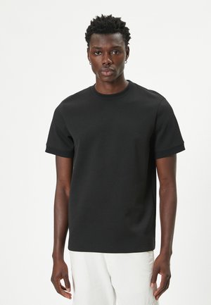 Sort kortærmet T-shirt i en blød bomuldsblanding, med rund hals og afslappet pasform, samt ribbet tekstur ved ærmerne og kanten.