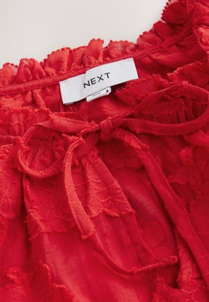 Červený čipkovaný top s jemnou textúrou, kvetinovým vzorom, nariaseným výstrihom a nastaviteľnou stiahnuteľnou páskou v páse. Značková etiketa s nápisom "NEXT".