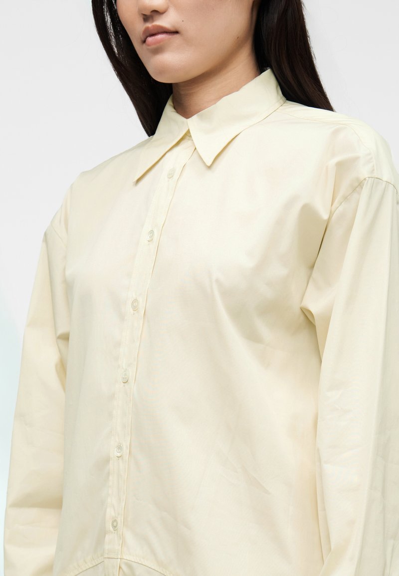 Chemise boutonnée jaune clair avec col classique et manches longues. Fabriquée dans un tissu lisse et léger avec une coupe décontractée.