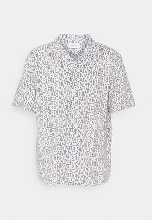 Biała koszulka polo z krótkim rękawem, ozdobiona czarnym nadrukiem tekstowym "Calvin Klein" o różnych orientacjach oraz kołnierzykiem na guziki.