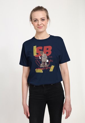 Námořnická modrá bavlněná tričko s grafickým designem a tučnou červenou typografií, doplněné ilustrací reproduktoru na skateboardu, zvýrazněné žlutou páskou.