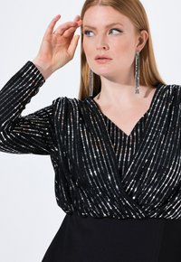 Černý top s dlouhými rukávy zdobený černými flitry, s vertikálními stříbrnými pruhy a výstřihem do V, spojený s jednobarevnou černou spodní částí.