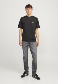 Svart bomulls T-skjorte med rund hals og korte ermer, med en liten hvit trykt logo på brystet, i kombinasjon med grå denim jeans.