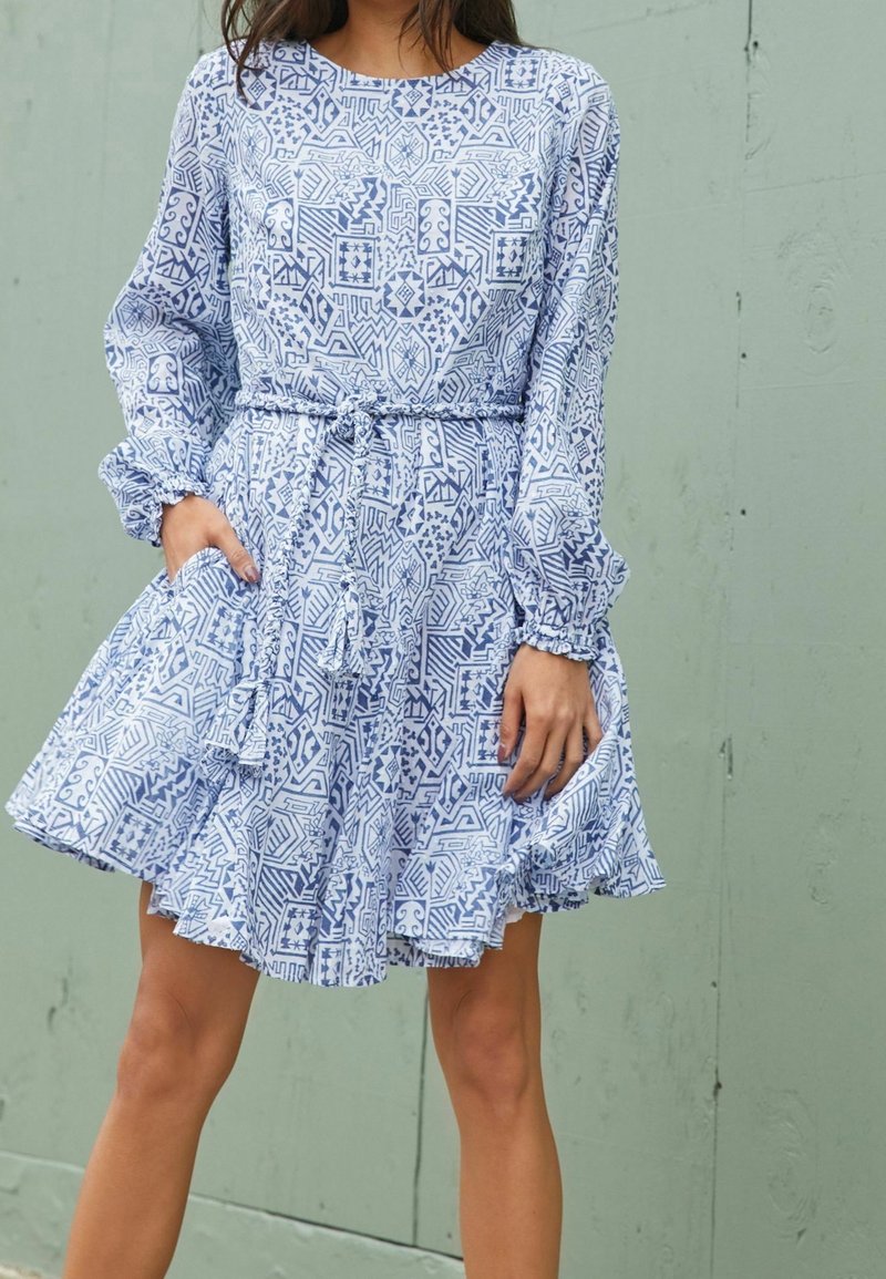 Robe bleu clair avec un motif, manches longues, ceinture à la taille et ourlet à volants. Le tissu semble doux avec une silhouette fluide.