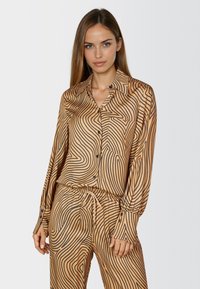 Brown satin blouse with black wavy lines, long sleeves, and button front. Features a collar and single chest pocket.