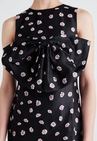 Black dress featuring small pink floral embroideries, with a large bow detailing on the front. Smooth fabric with a sleeveless design.