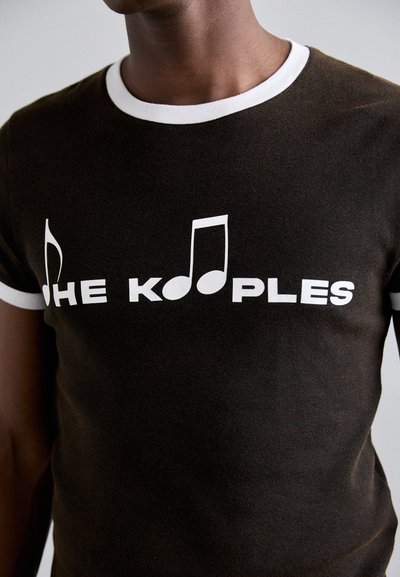 Smeđa pamučna majica s bijelim rebrastim okovratnikom. Sadrži natpis "THE KOOPLES" u podebljanim bijelim slovima i grafiku nota.