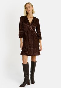 Vestido envolvente de estampado de leopardo marrón con mangas abullonadas largas y una falda acampanada, combinado con botas de tacón marrones hasta la rodilla. Textura de tela suave.