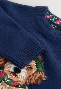 Marineblau gestrickter Pullover mit gerippten Ärmelbündchen. Verfügt über ein detailliertes Hundedesign mit einem grünen Hut, gefertigt aus weichem, strukturiertem Stoff.