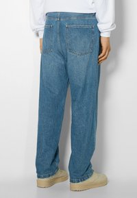 Pantalones vaqueros de mezclilla azul claro con un corte relajado, que cuentan con una cintura alta, dos bolsillos traseros y costuras visibles. Llevados con zapatos beiges.