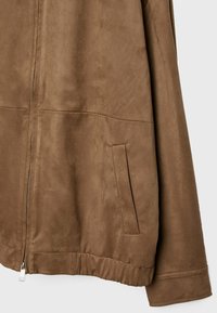Chaqueta de ante sintético marrón con cierre de cremallera, bolsillos laterales y dobladillo fruncido en la parte inferior, con una textura suave y mate.