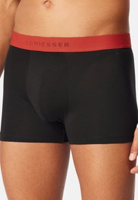 Boxer in cotone nero con elastico rosso sulla vita con il logo "SCHIESSER". Design aderente e texture morbida.