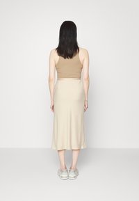 Débardeur beige sur une longue jupe beige. Texture lisse, silhouette ajustée. Porté avec des baskets grises. Design simple, peu de détails.