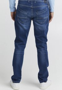 Jeans de denim azul oscuro de corte slim, con bolsillos traseros y detalles de costura sutil. Complementados con zapatillas blancas.