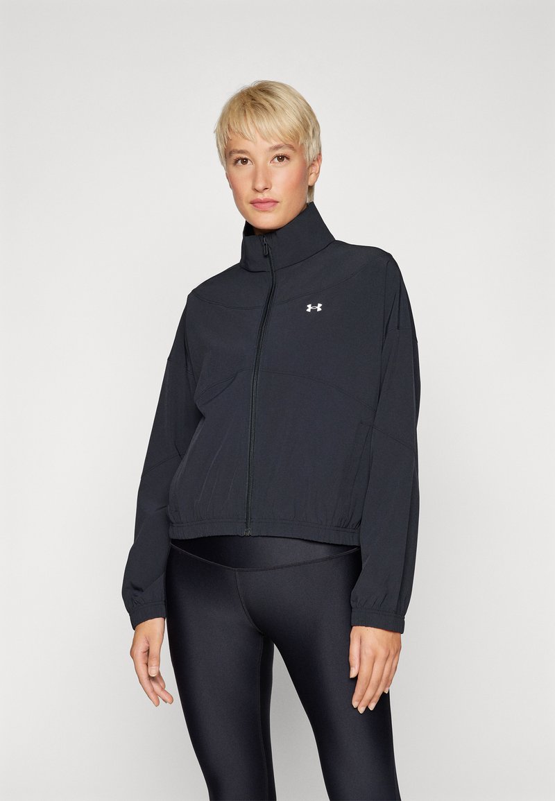 Chaqueta deportiva negra con collar alto, cremallera frontal y mangas largas. Fabricada con un material liviano. Presenta un logo de Under Armour en el pecho.
