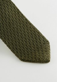 Oliwkowy krawat z teksturowanym, plecionym wzorem; wąski kształt; i spiczasty koniec, wykazujący subtelny blask i detale.